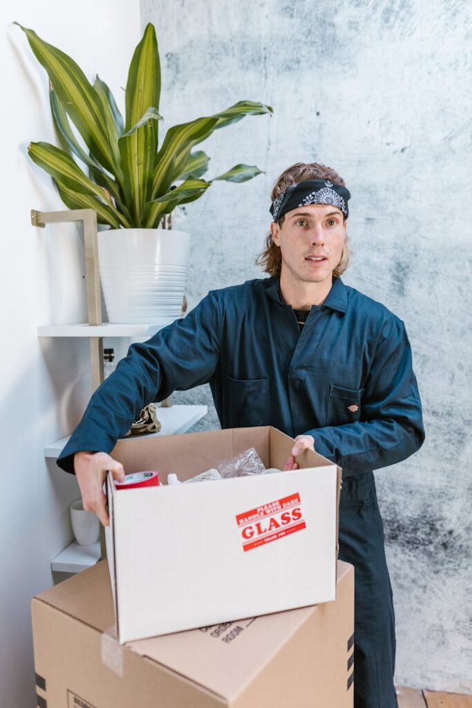 Worker in blue uniform with bandana handling a fragile package at home.