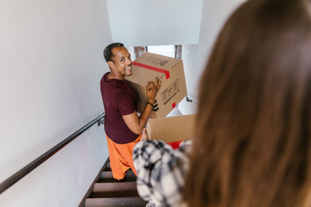 Crafting Captivating Headlines: Your awesome post title goes here An adult man smiling while carrying a moving box up staircase indoors.